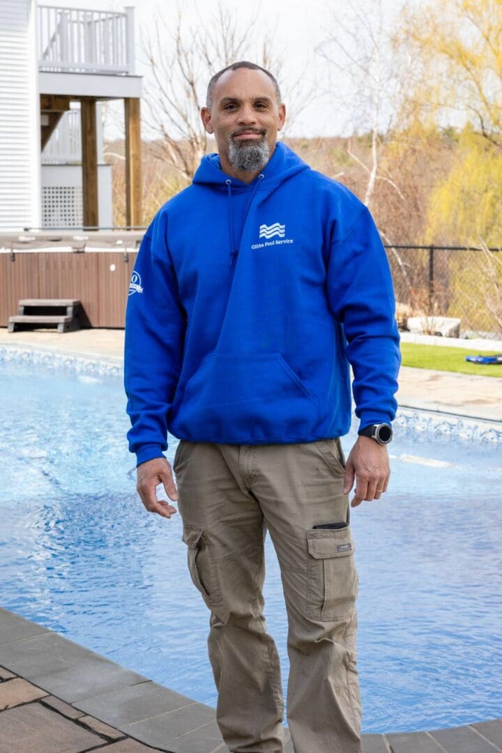 A man standing in front of a pool wearing a blue hoodie.