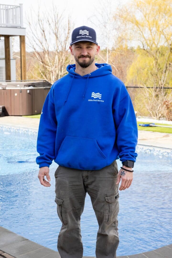 A man in blue hoodie and brown pants standing next to pool.