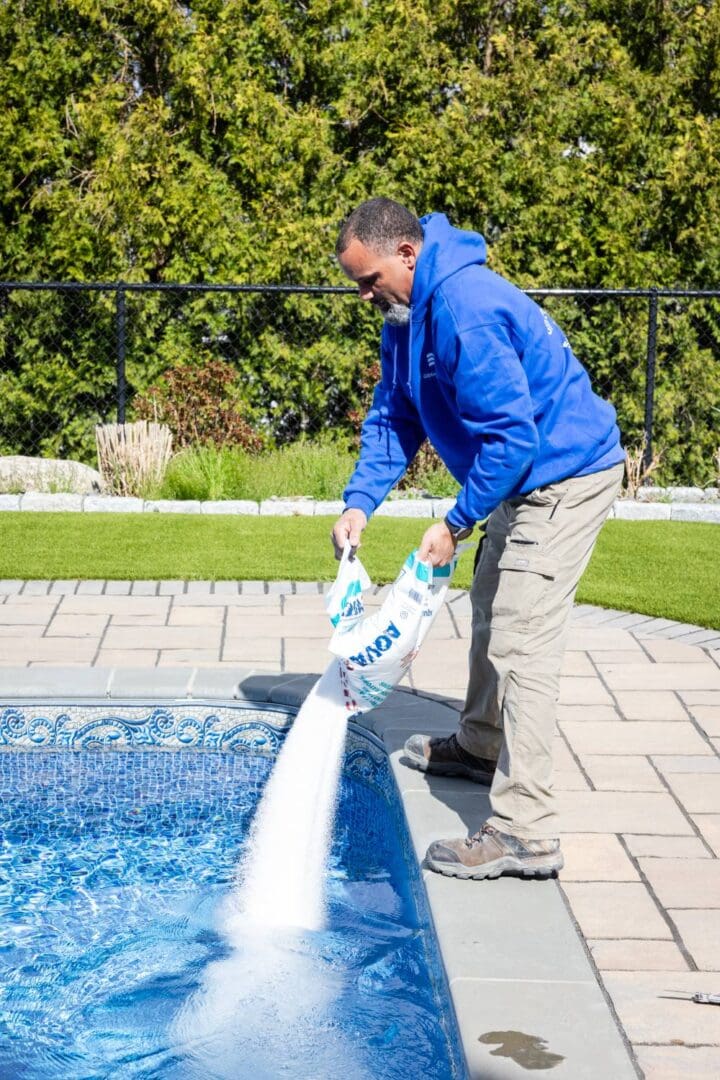 A man in blue jacket spraying water from pool.