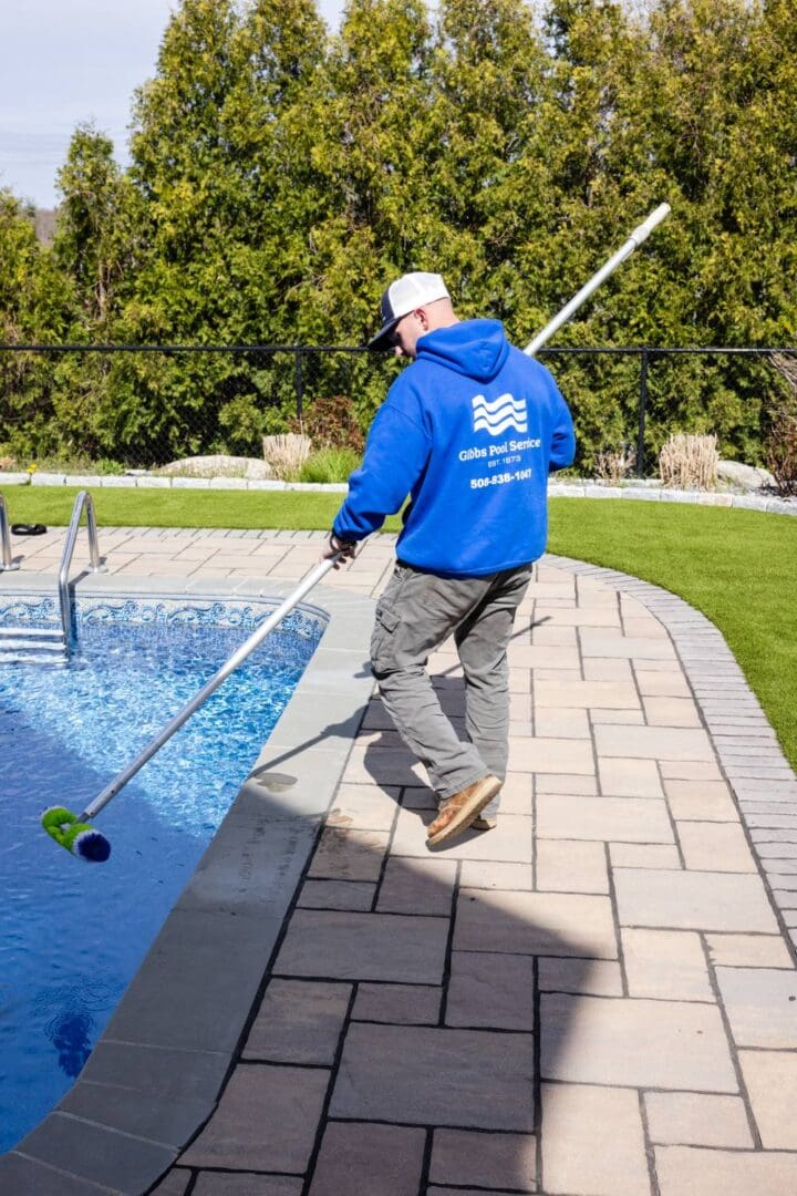 A man in blue jacket holding a pole near pool.