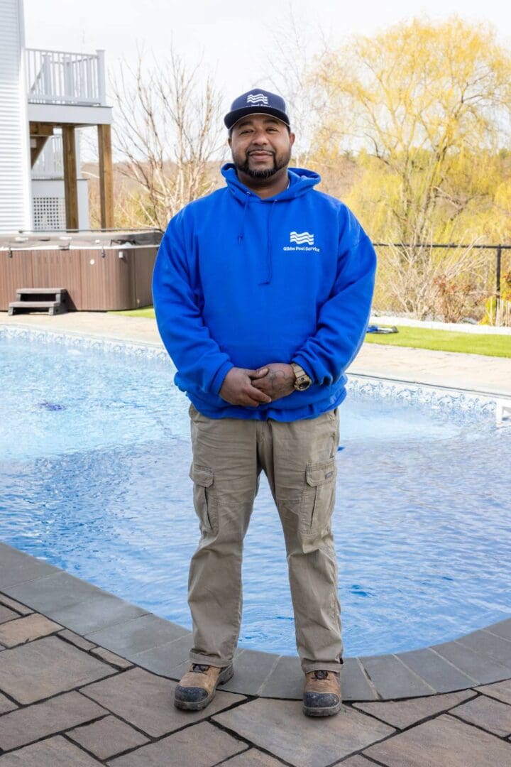 A man standing in front of a pool wearing a blue jacket.