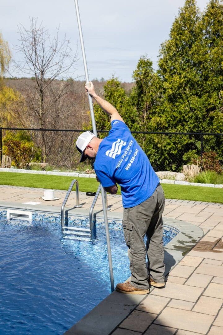 A man in blue shirt cleaning pool with pole.