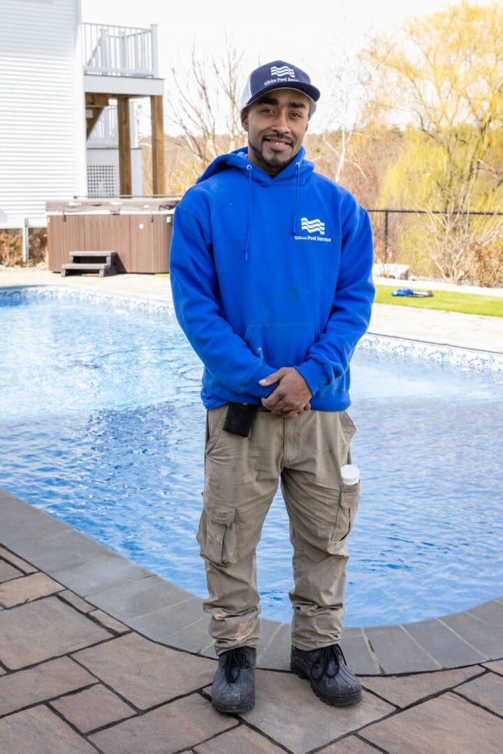 A man standing in front of a pool wearing a blue sweatshirt.
