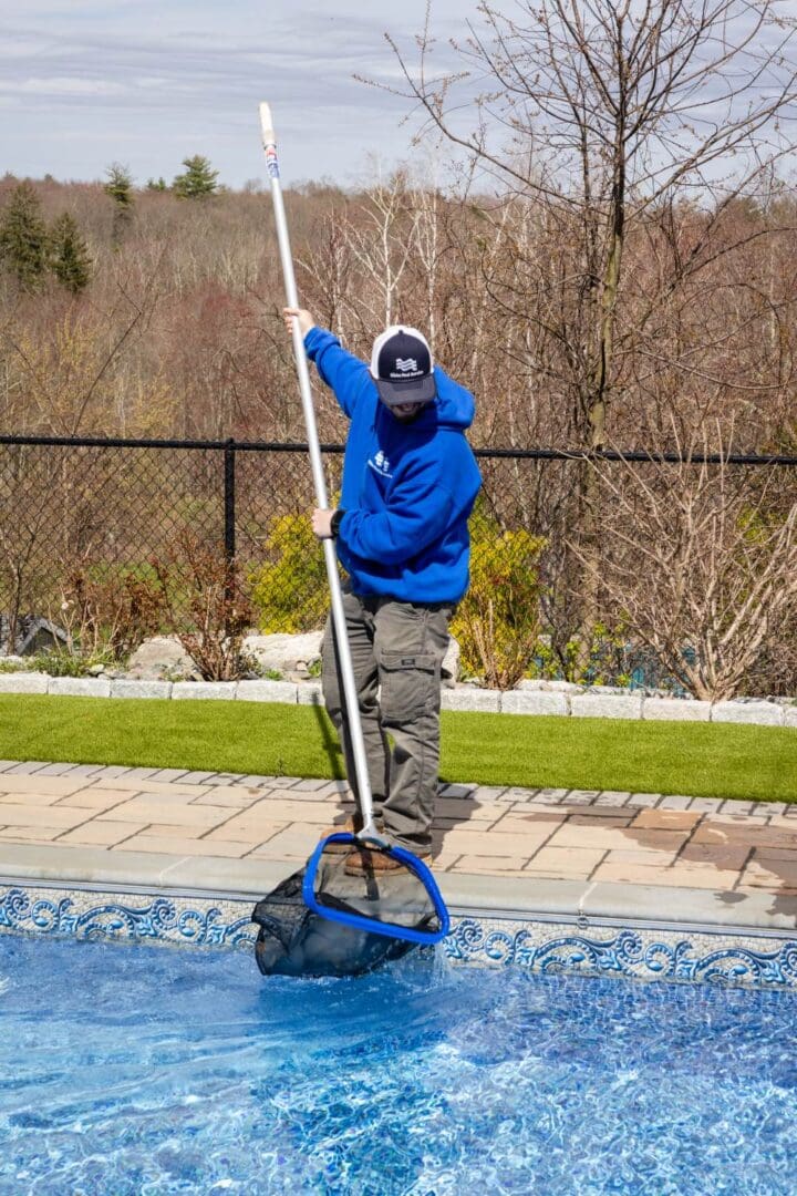 A man in blue jacket cleaning pool with net.