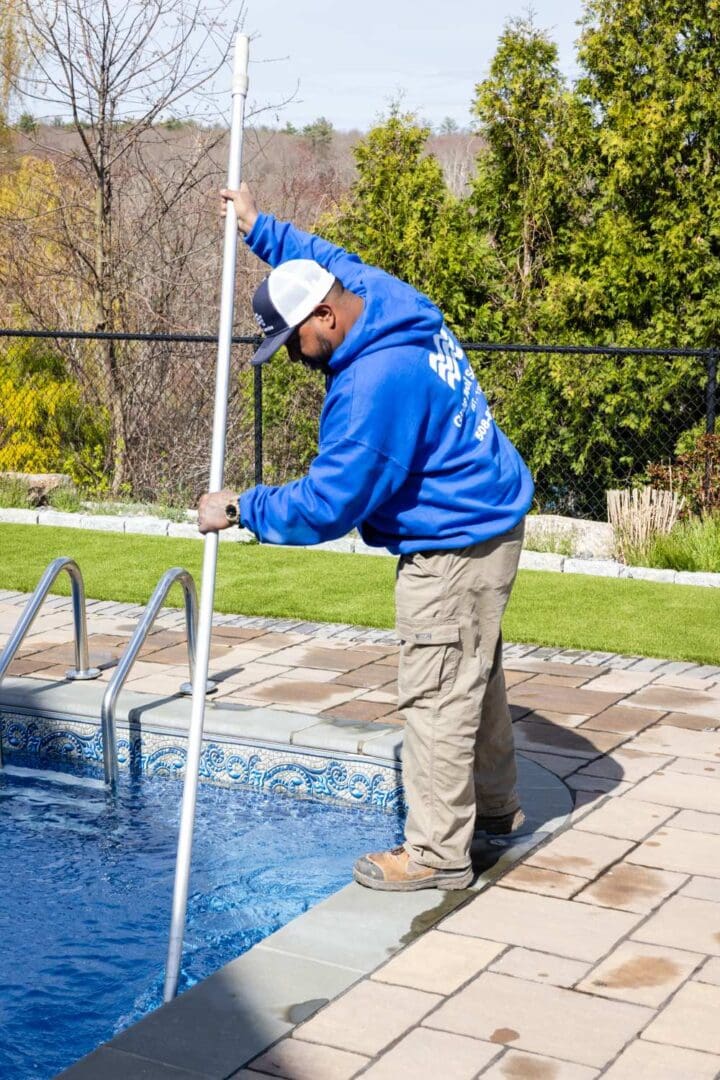 A man in blue jacket cleaning pool with white pole.