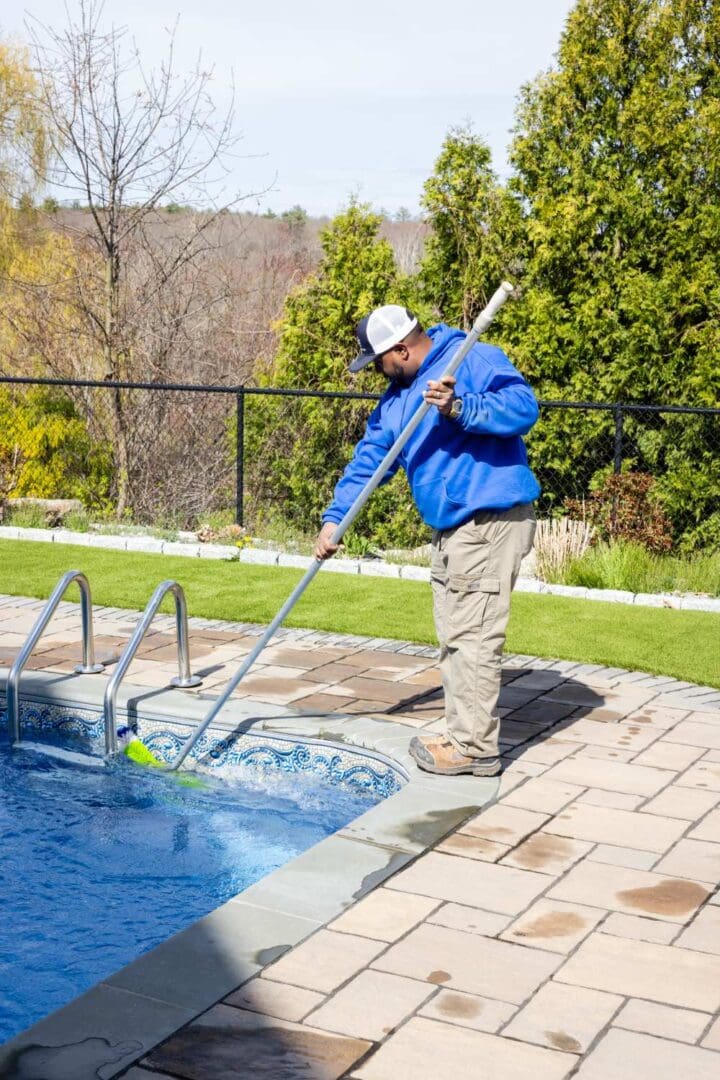 A man in blue jacket cleaning pool with a pole.