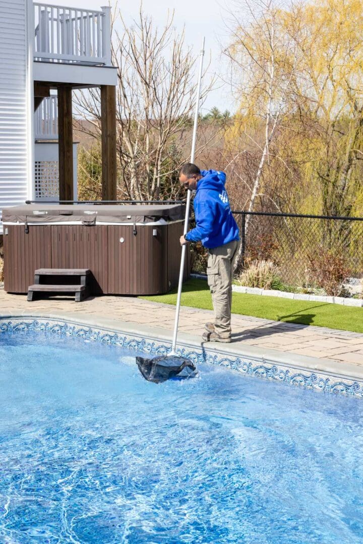 A man in blue jacket cleaning pool with pole.