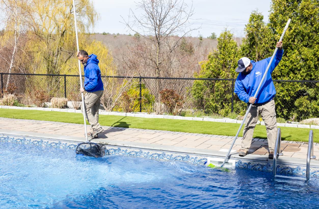 Two people cleaning a pool with mops and a ladder.