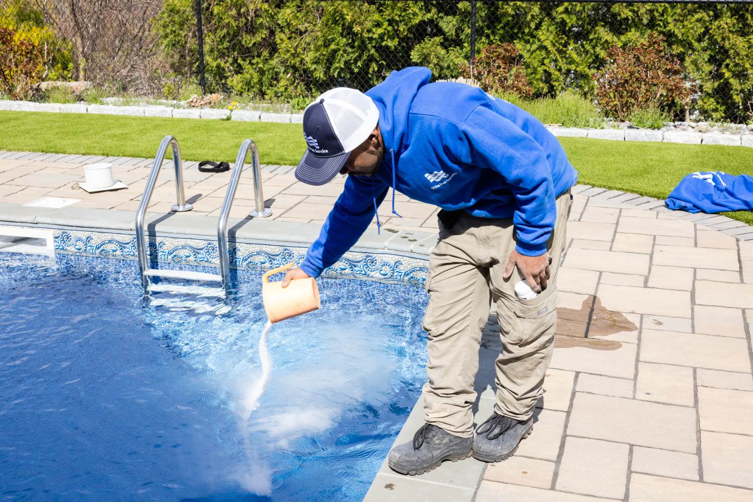 A man in blue jacket cleaning pool with spray.