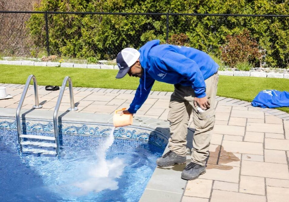 A man in blue jacket cleaning pool with water squirting out of it.